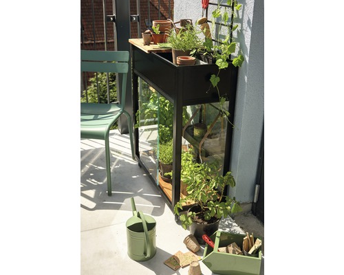 Balkonszene mit Hochbeet, Kräutern, Gießkanne und Gartengeräten.