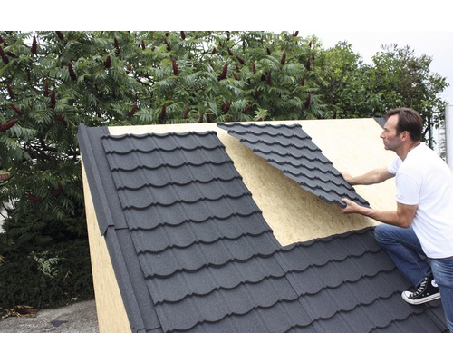 Un homme pose des tuiles métalliques sur un toit.