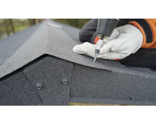 Une personne fixe des bardeaux de toiture avec un tournevis.