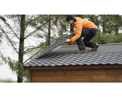 Un homme pose des tuiles de toit métalliques sur une maison en bois.