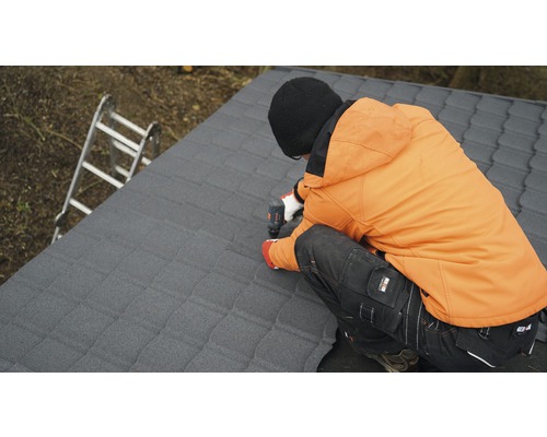 Un artisan fixe des plaques de toit avec un tournevis sans fil sur un toit