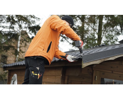 Un artisan monte du roofing sur une cabane de jardin avec une visseuse sans fil.