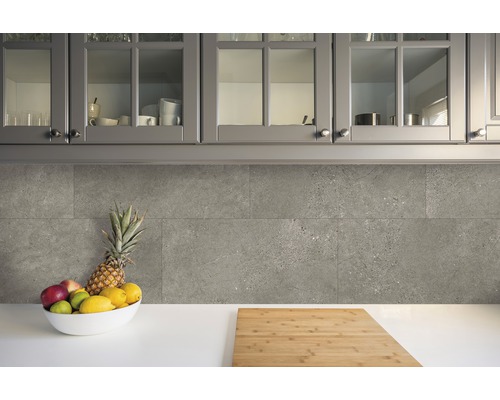 Scène de cuisine avec des carreaux muraux gris, un saladier de fruits et une planche à découper