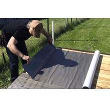 Eine Person verlegt eine Dachbahn auf einer Holzkonstruktion.