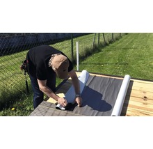 Ein Mann verlegt Dachpappe auf einem Holzboden im Freien.