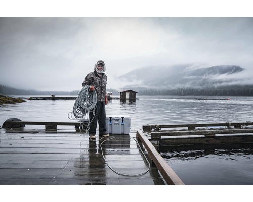 Mann mit Seil auf einem Holzsteg am Wasser mit einer Kühlbox