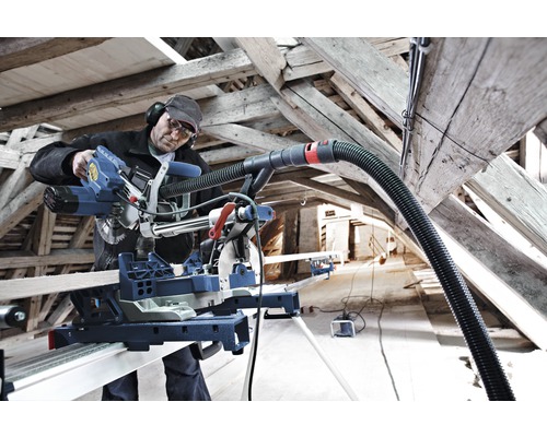 Une personne travaille avec une scie à onglet et un aspirateur dans une charpente.