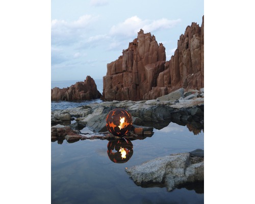 Boule à feu décorative en métal sur la rive avec des rochers et de l''eau.