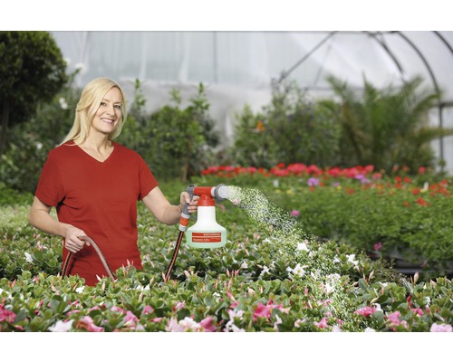 Femme arrosant des plantes avec un pulvérisateur de jardin dans une serre.