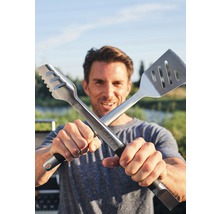 Mann hält Grillzange und Grillwender gekreuzt in die Kamera.