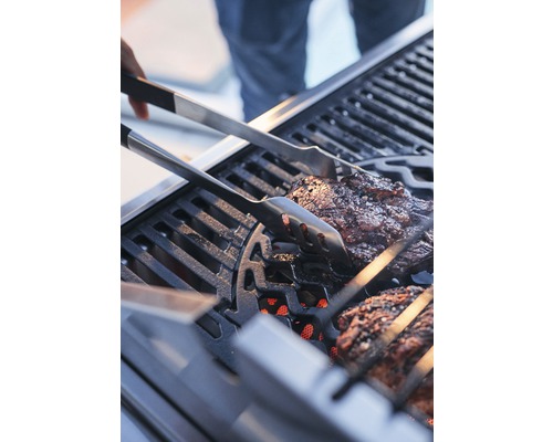 De la viande est retournée sur un grill à l''aide d''une pince à barbecue.