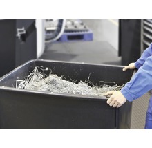 Une personne tient une cuve noire remplie de copeaux de métal.