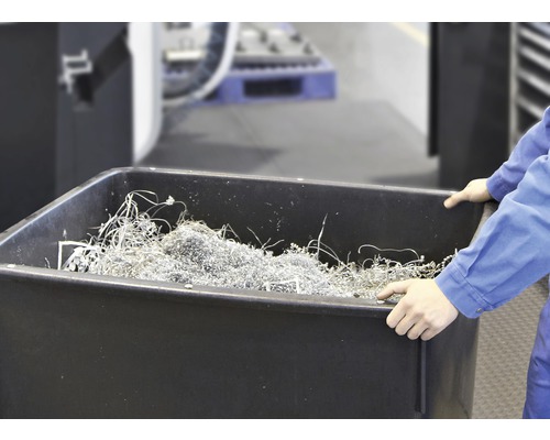 Une personne tient une cuve noire remplie de copeaux de métal.