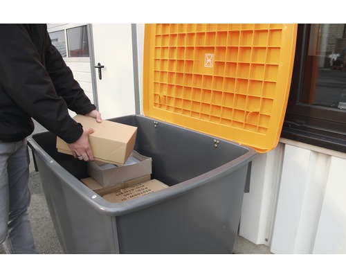 Une personne dépose des paquets dans une poubelle de recyclage grise avec un couvercle orange ouvert