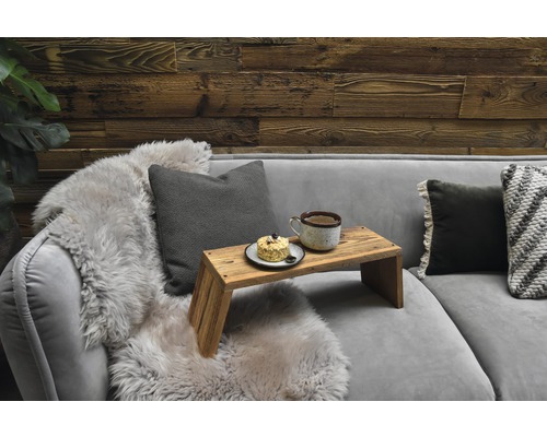 Canapé gris avec coussins, fourrure et plateau de service avec tasse et gâteau devant un mur en bois