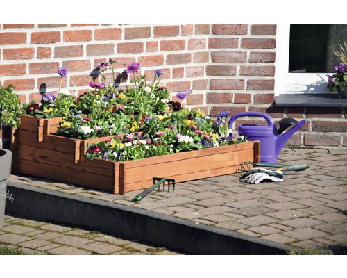 Jardinière étagée en bois avec fleurs, arrosoir et outils de jardin devant un mur de briques