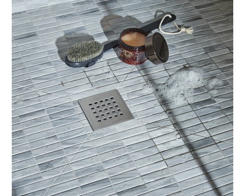 Gros plan d''une douche avec carrelage au sol, siphon de douche, brosse, additif pour le bain et mousse de savon