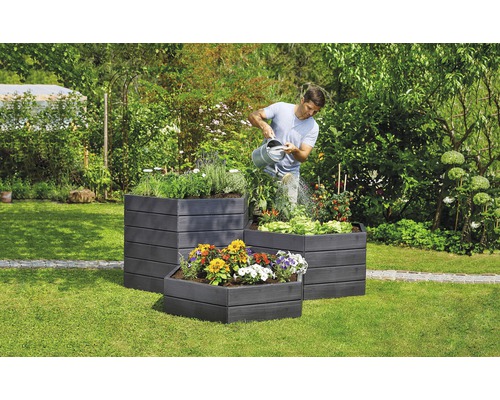 Mann giesst Pflanzen in drei Hochbeeten im Garten.