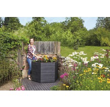 Frau bepflanzt ein sechseckiges Hochbeet aus Holz im Garten.