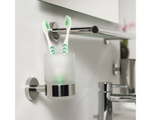 Support mural avec gobelet à brosse à dents en verre et deux brosses à dents dans la salle de bain.