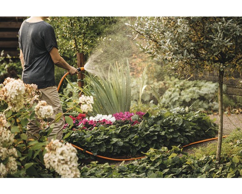 Eine Person giesst mit einem Gartenschlauch Blumen im Garten.
