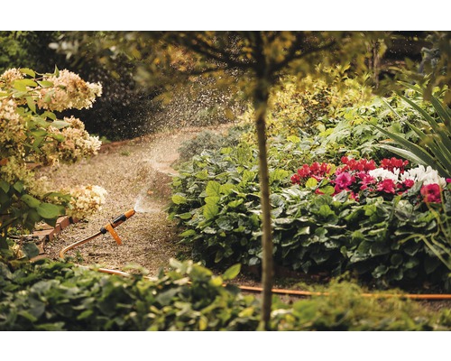Gartenszene mit Blumen und einer Bewässerungsanlage, die Wasser sprüht.