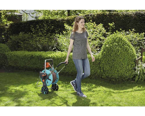 Femme tirant un chariot de tuyau d''arrosage sur une pelouse.