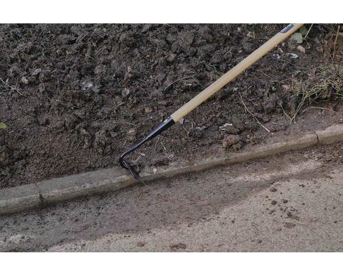 Houe de jardin avec manche en bois utilisée à côté d''une bordure de trottoir