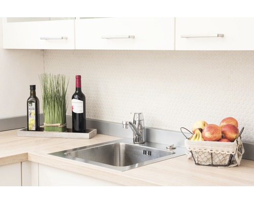 Küchenspüle aus Edelstahl mit Armatur, umgeben von Dekoration und Lebensmitteln.