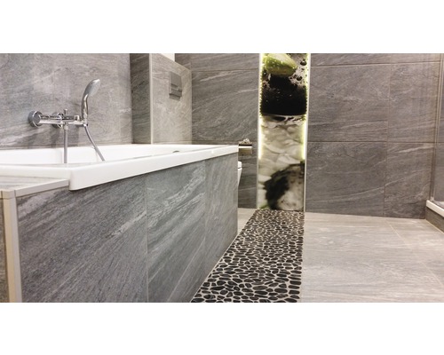 Badezimmer mit Badewanne, grauen Fliesen und Kieselboden