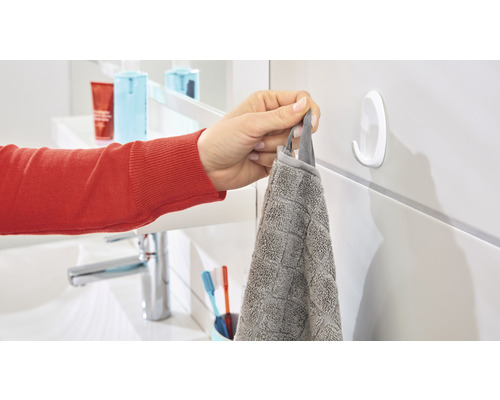 Une personne accroche une serviette grise à un crochet adhésif blanc dans la salle de bain