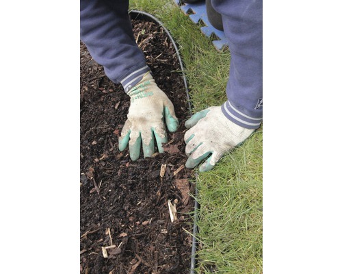 Des mains gantées travaillent sur une bordure de parterre entre la terre et la pelouse.