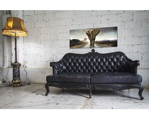 Dekorative Szene mit Stehlampe, Ledersofa und Wandbild mit Elefantenmotiv vor einer Ziegelwand