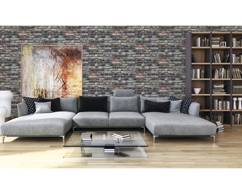 Wohnzimmer mit grauer Couch, Bücherregal und Wand in Ziegeloptik.