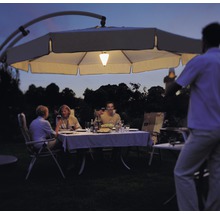 Szene mit einer Gruppe von Personen, die im Garten unter einem beleuchteten Sonnenschirm sitzen und essen.