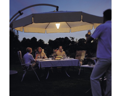 Szene mit einer Gruppe von Personen, die im Garten unter einem beleuchteten Sonnenschirm sitzen und essen.