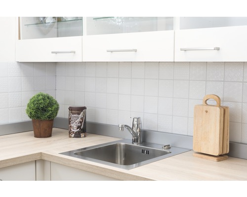 Scène de cuisine avec évier, robinet, planches à découper et décoration sur un plan de travail clair devant une crédence en carrelage blanc