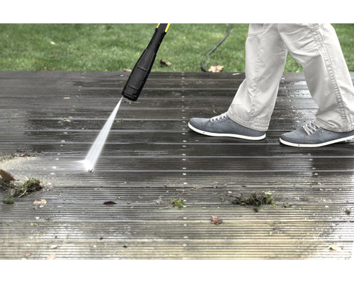 Eine Person reinigt eine Holzterrasse mit einem Hochdruckreiniger.