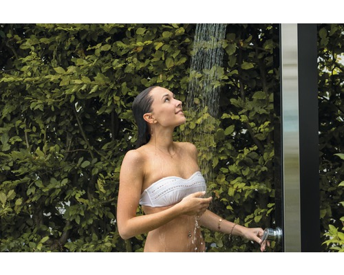 Femme sous douche de jardin avec des plantes vertes en arrière-plan