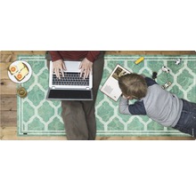Familie auf einem Teppich: Eine Person arbeitet am Laptop, während ein Kind daneben liegt und ein Buch anschaut, umgeben von Spielzeugautos.