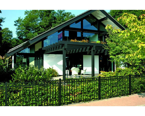 Modernes Haus mit Glasfassade, umgeben von einem schwarzen Zaun und üppigem Grün