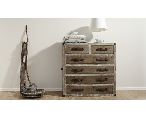 Commode avec tiroirs, lampe et décoration sur plancher en bois devant un mur
