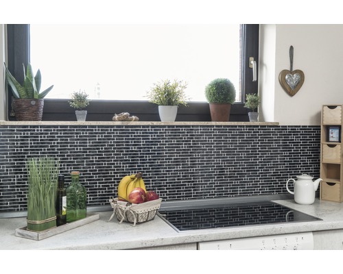 Scène de cuisine avec carreaux de mosaïque, rebord de fenêtre avec plantes, corbeille de fruits et plaque de cuisson.