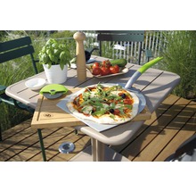 Szene mit Pizza auf Pizzaschieber, Pizzaschneider, Schneidebrett und Zutaten auf einem Gartentisch.