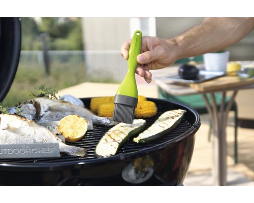 Mann bestreicht Gemüse und Fisch auf einem Grill mit einem Pinsel von Outdoorchef