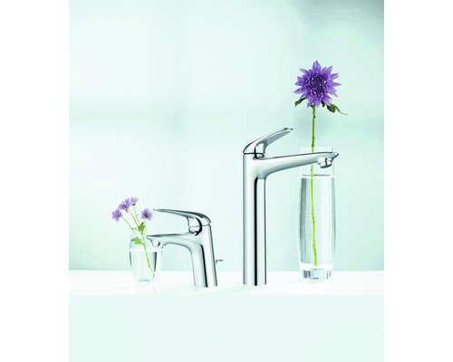 Zwei Waschtischarmaturen aus Metall unterschiedlicher Größe mit Blumen in Gläsern.