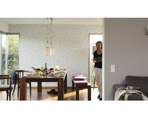 Salle à manger lumineuse avec table en bois, chaises, banc et papier peint fleuri.