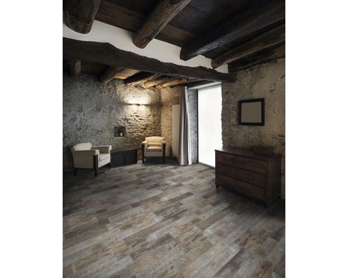 Pièce rustique avec plafond à poutres en bois, murs en pierre, plancher en bois, commode et fauteuils.