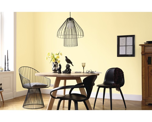 Salle à manger avec table ronde, chaises et suspension devant un mur jaune