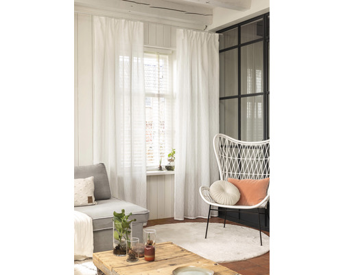 Salon avec canapé, fauteuil, table, tapis et rideaux blancs.